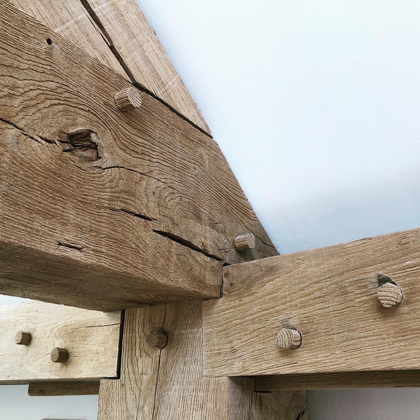Close-up of rustic wooden beams joined together with dowels, showing the wood’s natural grain, texture, and cracks against a white wall ceiling.